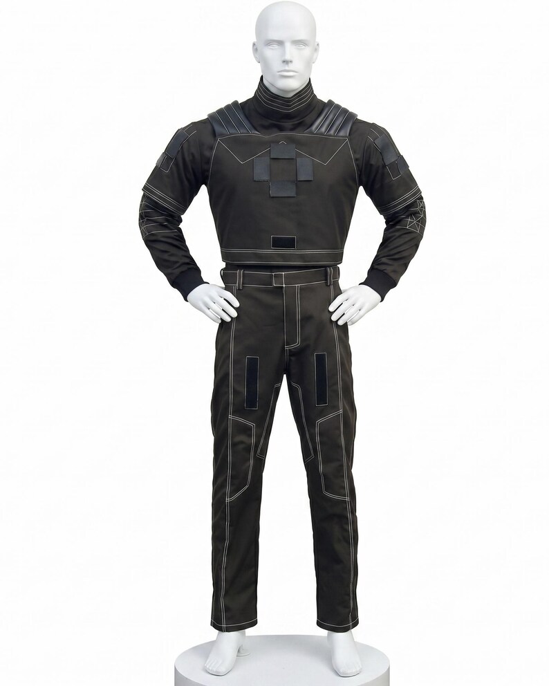 May include: A dark charcoal gray long-sleeved top and matching trousers set featuring white contrast stitching, a high collar, padded shoulder details, and rectangular black patches on the chest and thighs, displayed on a white mannequin.