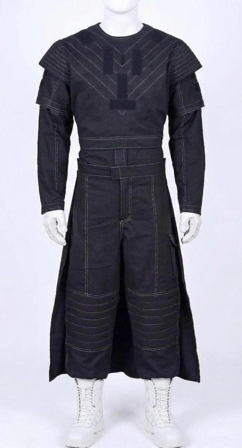 May include: A black long-sleeved tunic and matching trousers set featuring white contrast stitching. The top has a structured shoulder design and a central chest panel. The trousers include a wide waistband, side panels, and quilted knee sections.