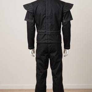 Pu&ograve; includere: Un completo nero composto da giacca a maniche lunghe e pantaloni abbinati con evidenti impunture bianche. La giacca presenta pannelli strutturati sulle spalle con dettagli a strati e una cucitura verticale sul retro. Pantaloni a gamba dritta.