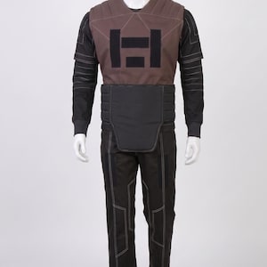 May include: A full-body costume displayed on a mannequin. The costume includes a brown vest with a black geometric design, a black long-sleeved shirt, black trousers, and a black belt. White stitching accents the seams.
