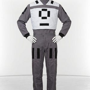 May include: A gray jumpsuit featuring a white chest panel with black rectangular accents. The garment includes long sleeves with black cuffs, a high collar, and matching gray trousers with white contrast stitching and black rectangular patches.