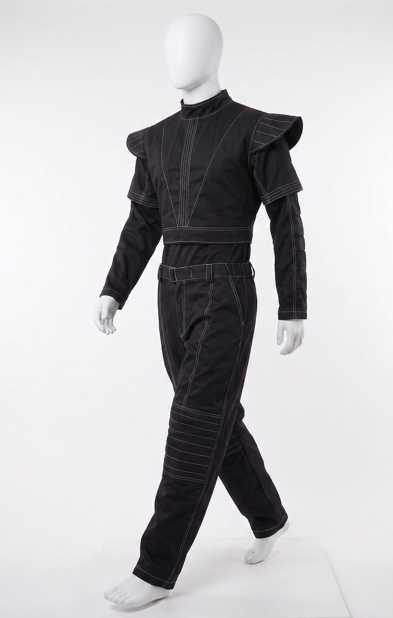 Pu&ograve; includere: Un completo nero a due pezzi composto da una maglia a maniche lunghe e pantaloni abbinati. La maglia presenta un colletto alto, spalline strutturate e cuciture bianche a contrasto. I pantaloni includono una cintura e dettagli trapuntati.