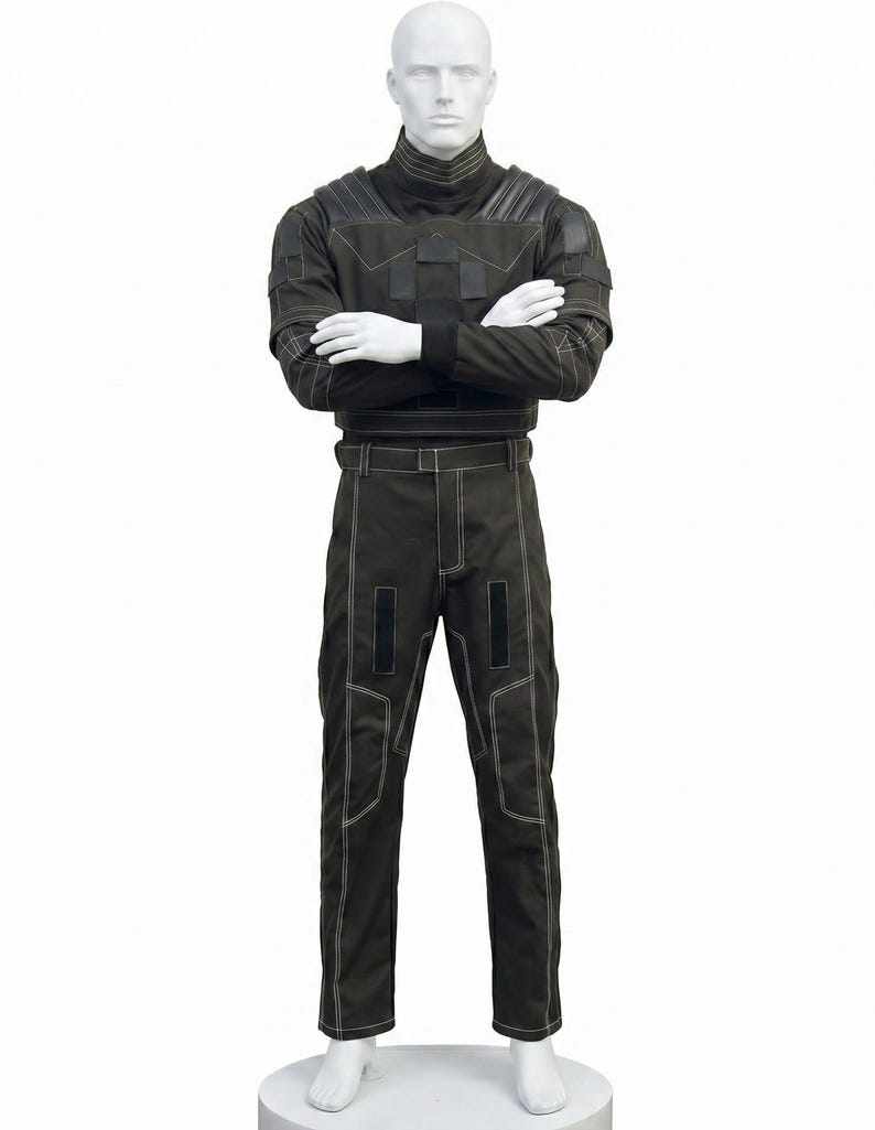 May include: A dark olive green tactical-style outfit consisting of a long-sleeved top with a high collar, shoulder padding, and matching trousers. The garment features prominent white contrast stitching, rectangular black patches, and a belt.