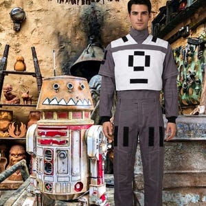 May include: A grey jumpsuit with a white chest panel featuring black rectangular accents, paired with grey boots. Beside the jumpsuit stands a weathered, cylindrical droid with a red and white paint finish, featuring a jagged tooth pattern.