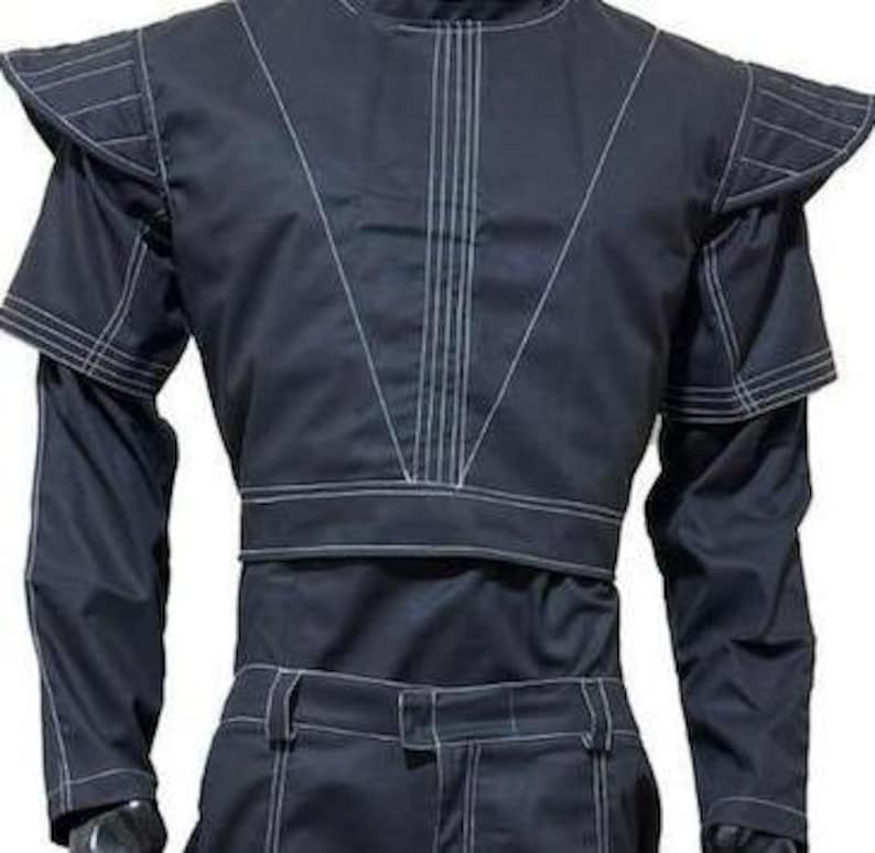 Pu&ograve; includere: Un completo composto da giacca a maniche lunghe e pantaloni blu scuro con evidenti cuciture bianche a contrasto. La giacca presenta spalline strutturate, un colletto alto e un design corto sul busto con linee verticali impunturate.