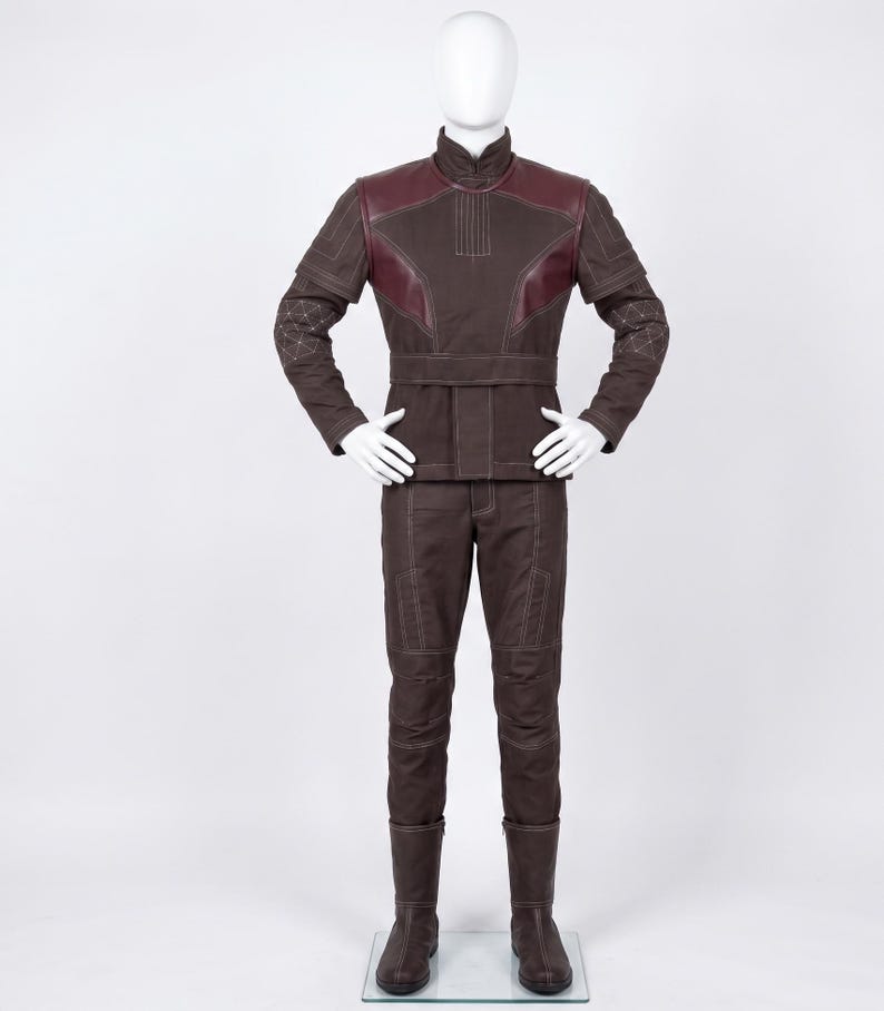 May include: A dark brown long-sleeved jacket and matching trousers set on a mannequin. The jacket features a high collar, a wide waist belt, and dark red shoulder panels. The sleeves and pants have white topstitching and geometric patterns.