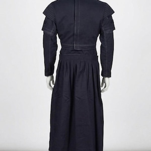 May include: A dark navy blue ensemble consisting of a cropped jacket with structured shoulders and long sleeves, paired with a high-waisted, floor-length pleated skirt. The garment features visible white contrast stitching throughout the design.