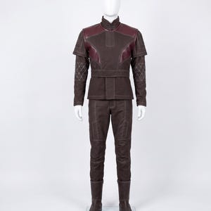 May include: A dark brown long-sleeved jacket and matching trousers set featuring a high collar, burgundy shoulder panels, and white contrast stitching. The sleeves include a geometric quilted pattern, and the jacket has a structured waist belt.