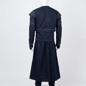 May include: A dark navy blue long-sleeved tunic and matching floor-length skirt set featuring prominent white topstitching. The tunic has a layered shoulder design and a vertical seam down the back, while the skirt is pleated and full-length.
