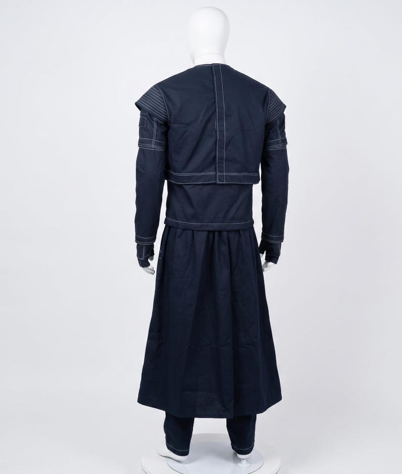 May include: A dark navy blue long-sleeved tunic and matching floor-length skirt set featuring prominent white topstitching. The tunic has a layered shoulder design and a vertical seam down the back, while the skirt is pleated and full-length.