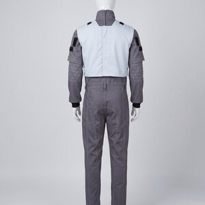 May include: A gray jumpsuit featuring a light gray vest overlay, a high collar with a back zipper, long sleeves with quilted patterns on the forearms, black cuffs, and black rectangular patches on the shoulders, displayed on a white mannequin.