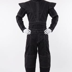Pu&ograve; includere: Un completo nero composto da un top corto a maniche lunghe e pantaloni abbinati. Il top presenta un colletto alto, spalline strutturate e cuciture bianche a contrasto. I pantaloni hanno un taglio dritto con dettagli di cuciture bianche.