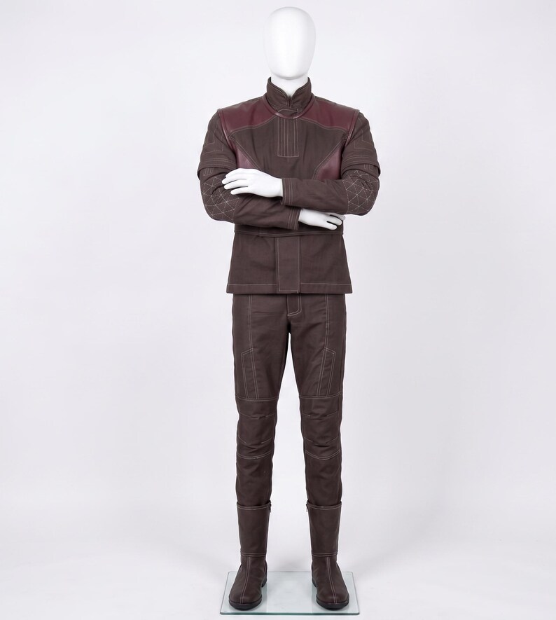 May include: A dark brown long-sleeved jacket and matching trousers set featuring a high collar, quilted sleeve detailing, and dark maroon shoulder panels. The outfit includes visible light-colored stitching throughout and dark brown boots.