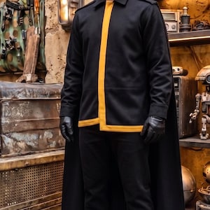 May include: A black jacket with a yellow vertical stripe, black trousers, a black cape, and black gloves. The jacket features a collared neckline and long sleeves. The ensemble is completed with black leather boots that have a thick, light brown sole.