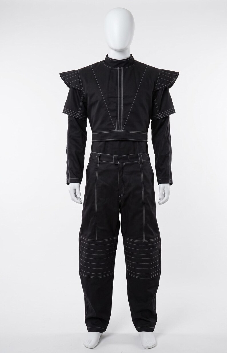 Pu&ograve; includere: Un completo nero composto da un top corto a maniche lunghe e pantaloni abbinati. Il top presenta un colletto alto, spalline strutturate e cuciture bianche a contrasto. I pantaloni includono passanti per cintura e cuciture orizzontali bianche.