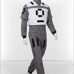 May include: A gray long-sleeved jumpsuit featuring a white chest overlay with black rectangular accents. The garment includes a high collar, black ribbed cuffs at the wrists and ankles, and additional black rectangular patches on the pants and sleeve.