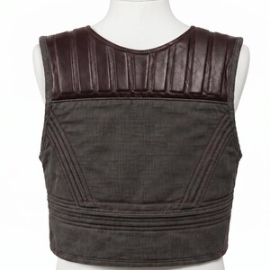 Peut inclure: Un gilet sans manches doté d'un panneau supérieur en similicuir marron foncé avec des surpiqûres verticales. La partie inférieure est en tissu gris foncé avec des lignes de couture horizontales et diagonales renforcées.