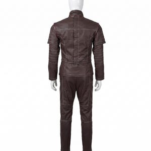 May include: A dark brown jacket and matching trousers set featuring a high collar, short sleeves with layered shoulder detailing, and prominent white topstitching throughout. The garment displays a structured design with horizontal paneling on the sleeves.