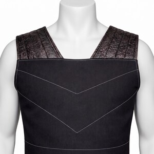 May include: A black sleeveless vest featuring a square neckline and wide shoulder straps with a dark brown textured finish. The main body of the vest is made of smooth black fabric with white topstitching forming two chevron patterns on the chest.