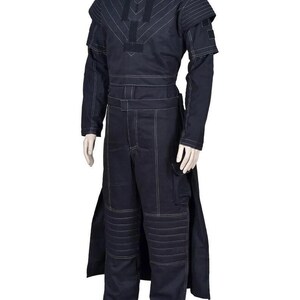 May include: A dark navy blue long-sleeved jumpsuit featuring white contrast stitching throughout. The garment includes a structured bodice with geometric paneling, padded shoulder details, and horizontal quilted sections on the knees.