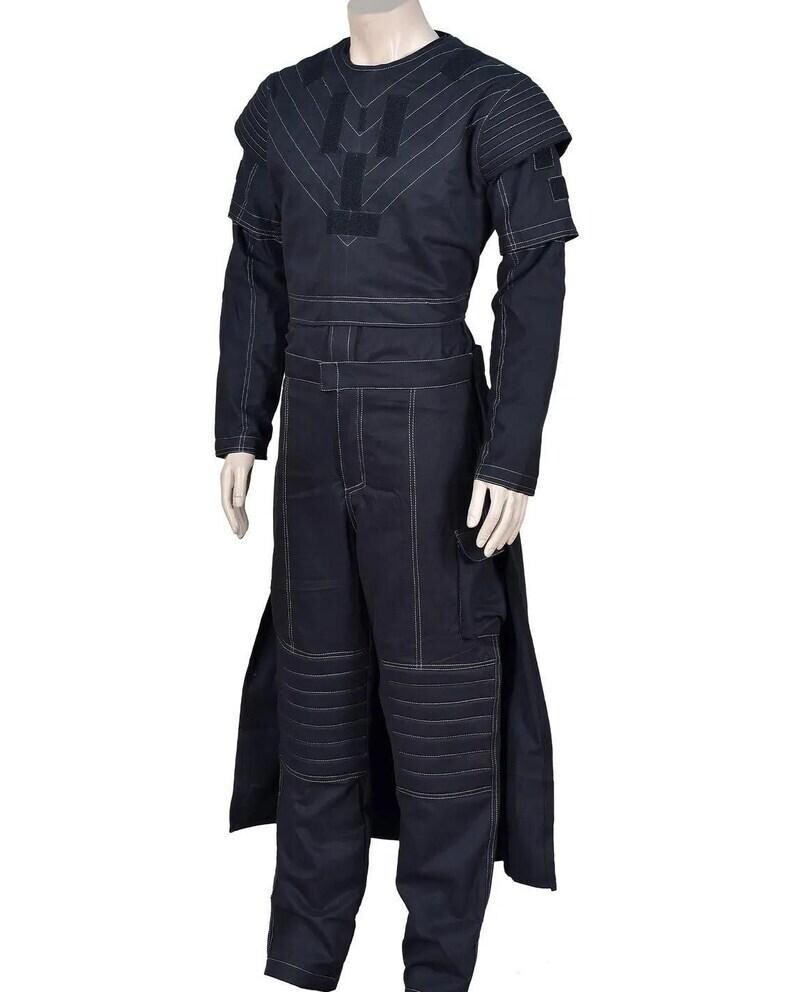 May include: A dark navy blue long-sleeved jumpsuit featuring white contrast stitching throughout. The garment includes a structured bodice with geometric paneling, padded shoulder details, and horizontal quilted sections on the knees.