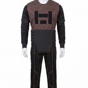 May include: A full costume on a mannequin. It features a brown vest with a black geometric design, a black long-sleeved shirt, black trousers, and a black belt. White stitching highlights the seams.