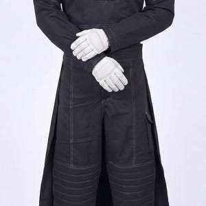 May include: A black long-sleeved tunic and matching trousers set featuring white contrast stitching, padded shoulder panels, and horizontal quilted detailing on the knees. The outfit is paired with white tactical gloves and white lace-up boots.