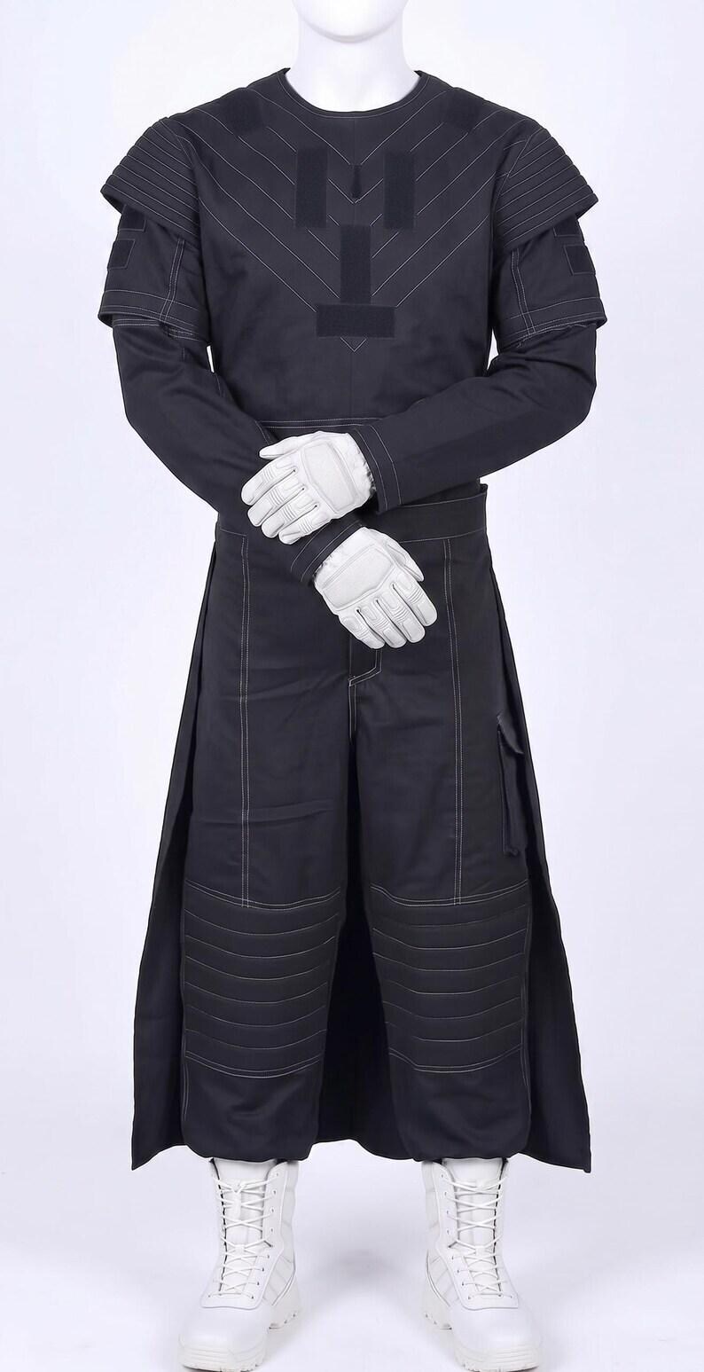 May include: A black long-sleeved tunic and matching trousers set featuring white contrast stitching, padded shoulder panels, and horizontal quilted detailing on the knees. The outfit is paired with white tactical gloves and white lace-up boots.