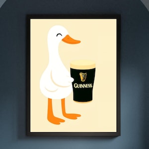 Puede incluir: Impresi&oacute;n enmarcada de un pato de dibujos animados sosteniendo una pinta de Guinness. El pato es blanco con pico y patas naranjas. El vaso de Guinness es negro con cabeza blanca y el logo de Guinness.