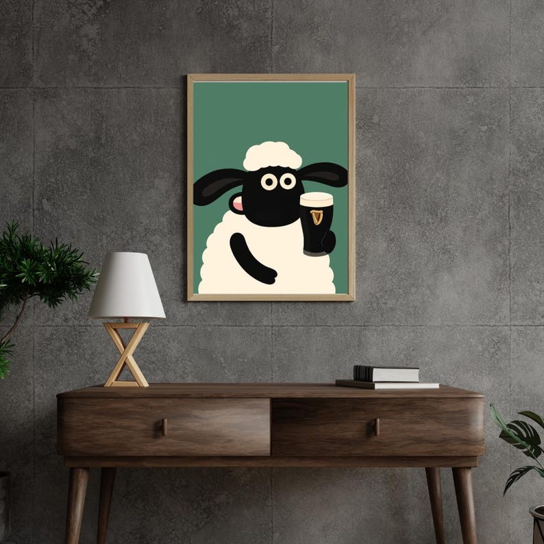 May include: Framed art print featuring a cartoon sheep holding a pint of Guinness. The sheep has a white body, black face and ears, and a white fluffy head. The background is a solid green color. The frame is a light brown color.