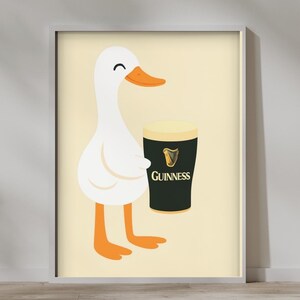 Puede incluir: Una impresi&oacute;n enmarcada con un pato de dibujos animados sosteniendo una pinta de Guinness. El pato es blanco con pico y patas naranjas. El vaso de Guinness es negro con espuma blanca y el logo de Guinness.