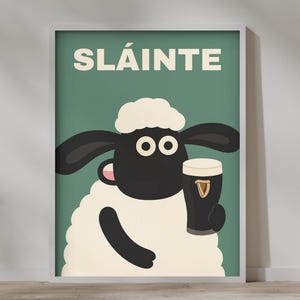 May include: A framed poster featuring a cartoon sheep holding a pint of stout. The sheep has a black face, ears, and arms, with a white fluffy body and head. The word "SL&Aacute;INTE" is printed in white on a green background.