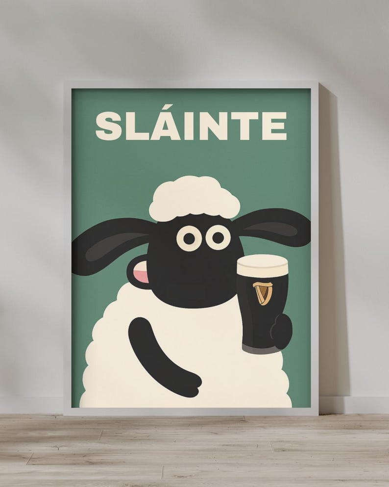 May include: A framed poster featuring a cartoon sheep holding a pint of stout. The sheep has a black face, ears, and arms, with a white fluffy body and head. The word "SL&Aacute;INTE" is printed in white on a green background.
