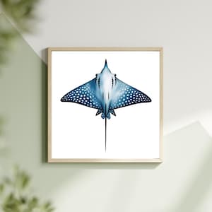Può includere: Una stampa artistica incorniciata con un'illustrazione di una manta aquila maculata blu. L'opera d'arte in stile acquerello mostra la forma e il motivo distintivi della manta su sfondo bianco. La cornice è in legno chiaro, aggiungendo un tocco naturale.