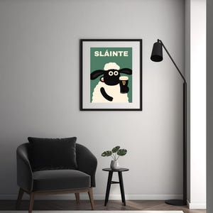 May include: A framed art print featuring a cartoon sheep holding a pint of stout. The print has the word "SL&Aacute;INTE" in green letters at the top. The sheep is black and white with a white fluffy body and a black frame.