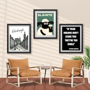 May include: Three framed art prints hang on a wall above two leather armchairs. The prints include a cityscape of Edinburgh, a cartoon sheep with a pint, and a quote by Richard Branson. The chairs have wooden frames and a small table.