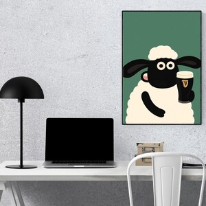 May include: A framed cartoon print featuring a sheep holding a pint of stout. The sheep has a white body, black face and ears, and is set against a green background. The pint glass has the Guinness logo. The print is displayed on a wall above a desk.