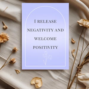 May include: A rectangular card with a light purple gradient background, featuring the text "I RELEASE NEGATIVITY AND WELCOME POSITIVITY" in black. The card is surrounded by dried flowers and foliage.