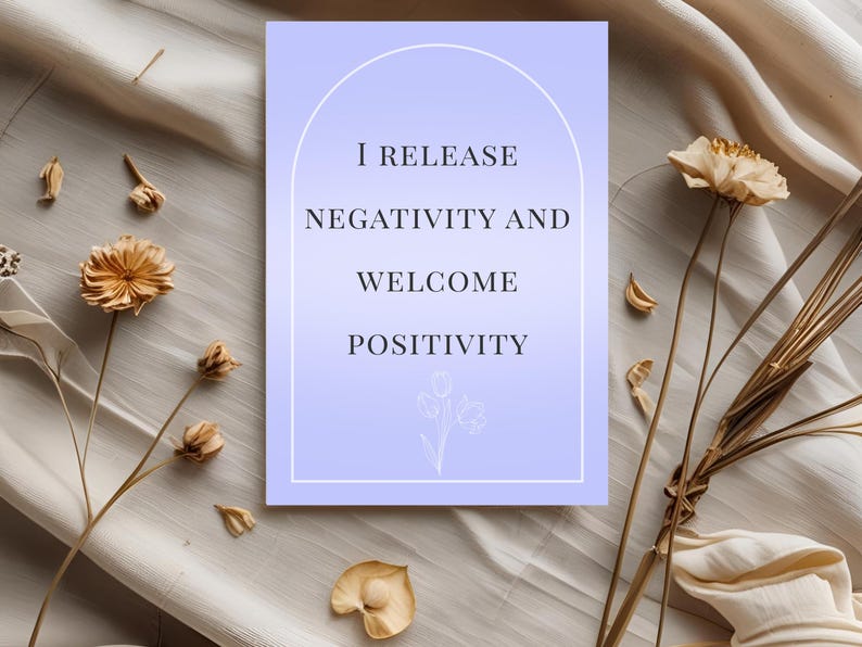 May include: A rectangular card with a light purple gradient background, featuring the text "I RELEASE NEGATIVITY AND WELCOME POSITIVITY" in black. The card is surrounded by dried flowers and foliage.