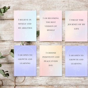 May include: Six affirmation cards with pastel gradient backgrounds and floral illustrations. Each card features a different positive affirmation in a white arch, such as "I believe in myself and my abilities."
