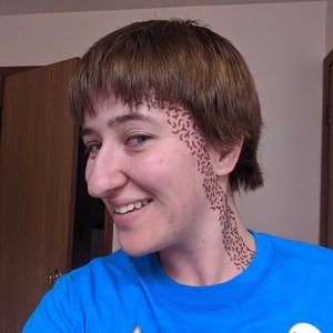 May include: A person wearing a blue t-shirt with a Star Trek badge and the text "I HAVE TO". The person has brown hair and a brown pattern on their face and neck. A button that says "SMOL" is also visible.