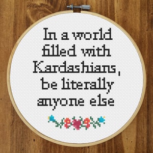 May include: White embroidery hoop with the text "In a world filled with Kardashians, be literally anyone else" in black. The hoop is decorated with a small floral design at the bottom.