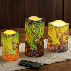 May include: Set of three battery-operated LED candles with a floral design reminiscent of Van Gogh's "Irises" painting. The candles feature a yellow glow and a remote control for operation. The design includes green leaves and purple flowers.
