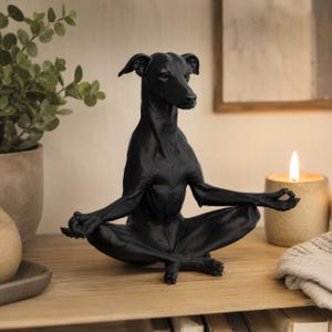 Op de afbeelding: Een matzwart beeldje van een Italiaanse windhond die in een gekruiste lotusmeditatiehouding zit. De hond heeft zijn voorpoten op de knieën rusten met de vingers gekruld in een mudra-gebaar, met een glad oppervlak en gedefinieerde oren.