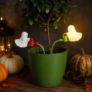 Puede incluir: Dos soportes para plantas con forma de fantasma en una maceta verde. Un fantasma blanco sostiene una regadera roja, mientras que el otro, un fantasma amarillo brillante, sostiene una regadera verde. Ambos unidos por tubos finos y transparentes.