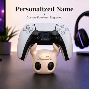 May include: A white and black game controller resting on a light-colored, horned character-shaped stand. The stand features the name ALEX embossed on the front. The text Personalized Name and Custom Forehead Engraving appear above the controller.