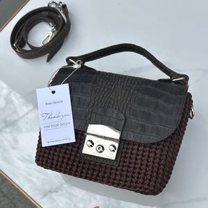 May include: A brown crocheted handbag with a dark brown crocodile-textured flap and silver hardware. The bag has a top handle and a detachable shoulder strap. A tag reads "Thank you for your order".