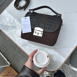 May include: A dark brown crocheted handbag with a dark grey crocodile-textured flap, a silver metal clasp, and a matching detachable shoulder strap. A white rectangular tag is attached, featuring the text From Ukraine, Thank you FOR YOUR ORDER.