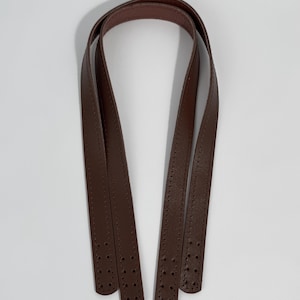 May include: A pair of dark brown bag handles made of smooth material with a matte finish. Each strap features a long, slender design with visible stitching along the edges and four pre-punched holes at each end for secure attachment to a bag.