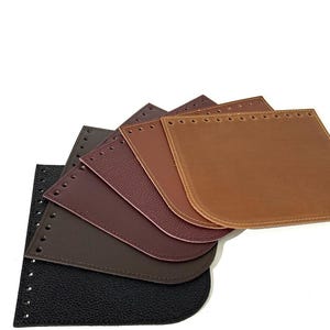 Puede incluir: Una colección de bases de bolsos de cuero en varios tonos de marrón, desde negro hasta marrón claro. Cada base es rectangular con esquinas redondeadas y agujeros pre-perforados para coser. Las texturas del cuero varían, ofreciendo opciones para la artesanía.